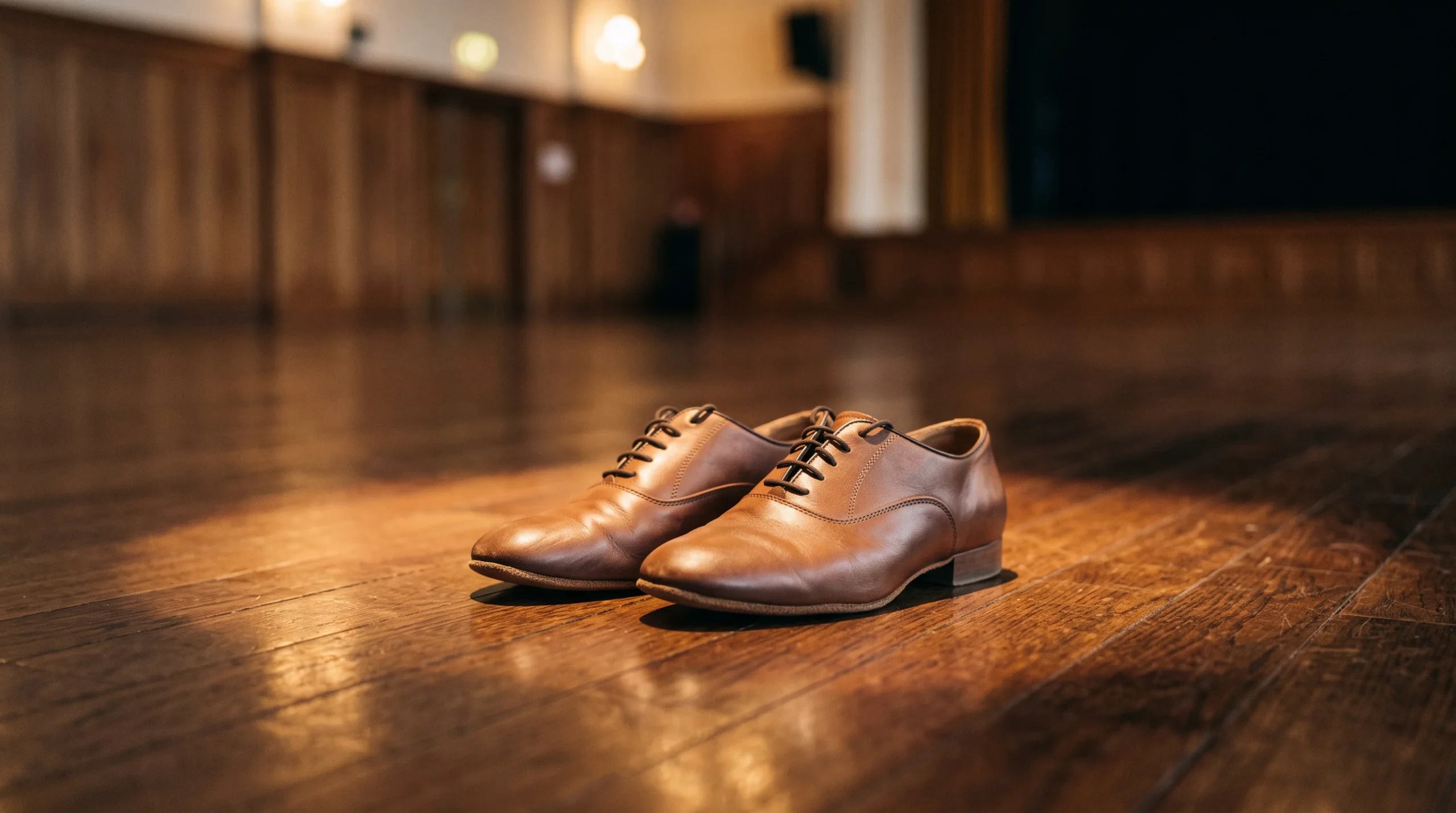 A pair of formal dance shoes on a wooden ballroom floor.