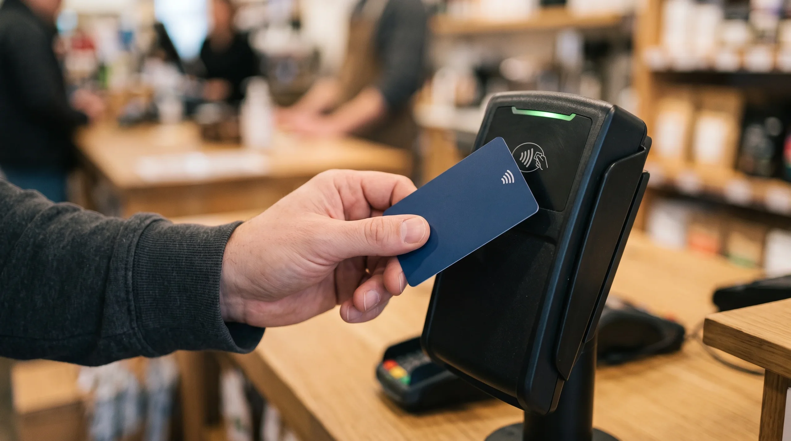 A person using a contactless payment card at a till terminal.