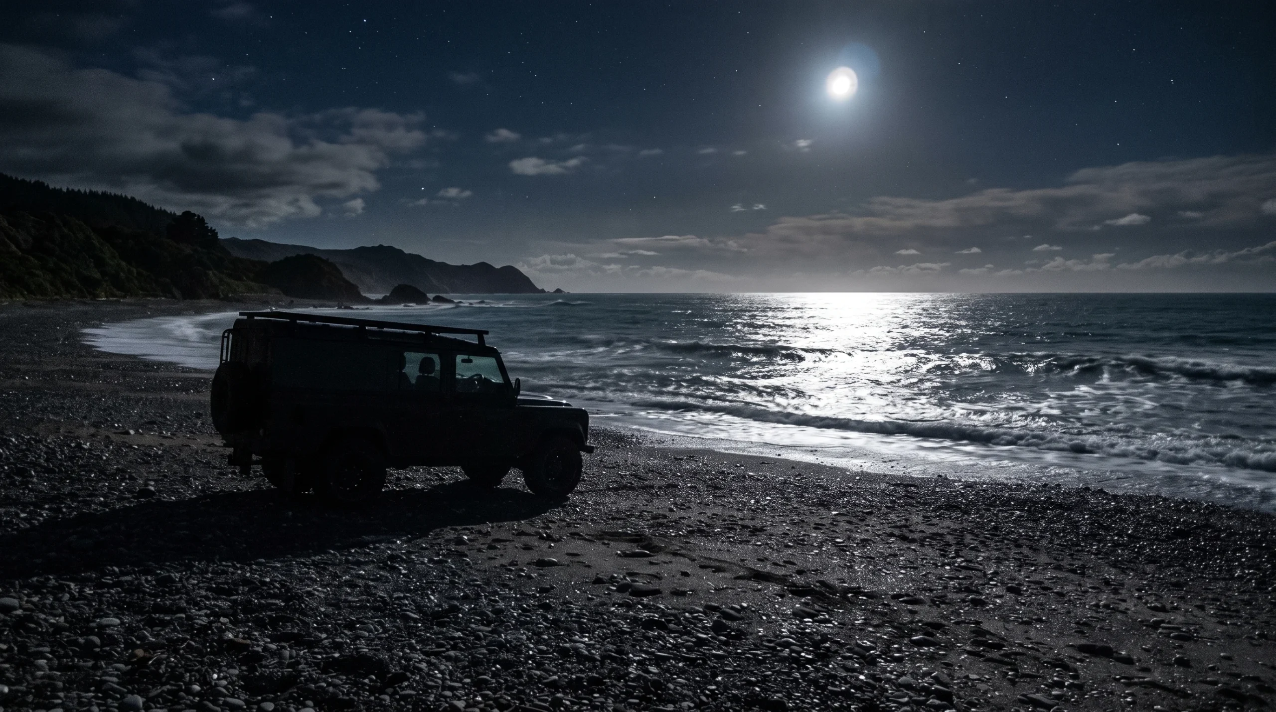 A generic utility vehicle on a shingle beach at night.